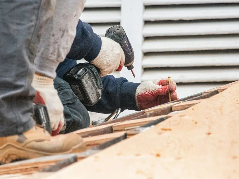 Operario con guantes atornillando con un taladro sobre un tablero de madera