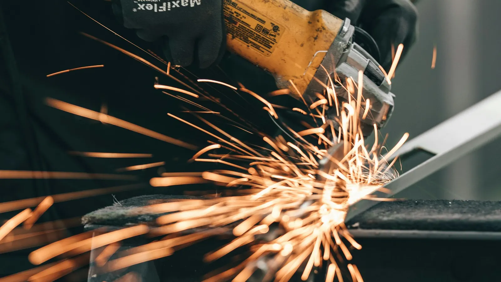 Operario con guantes cortando un perfil de metal con una radial que suelta chispas